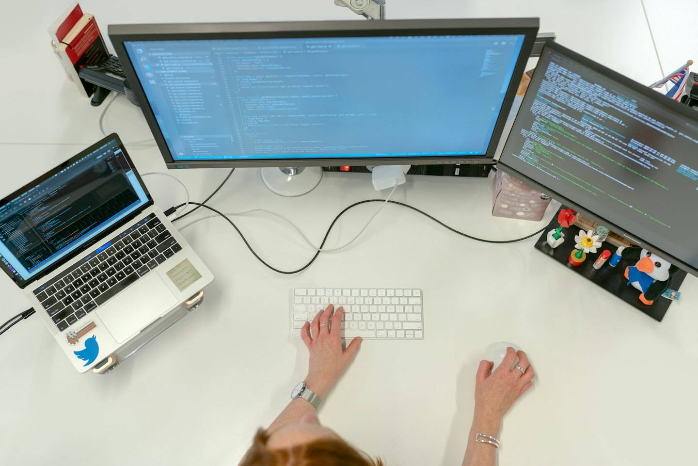 Programador escribiendo código en un puesto de trabajo con varios monitores en una oficina.